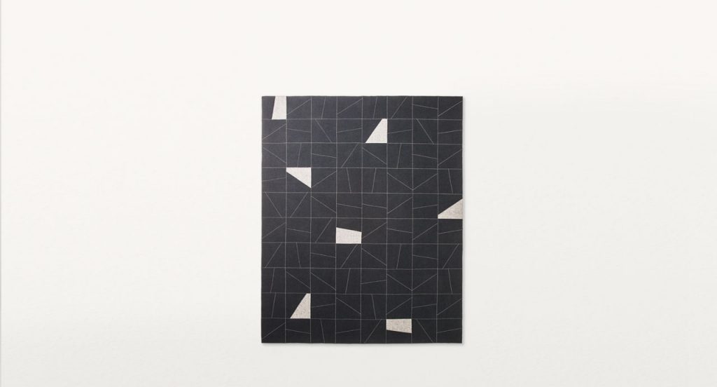 Rectangular Origami rug made of felt, squares and diagonal stitching in white and black colors on a white background.