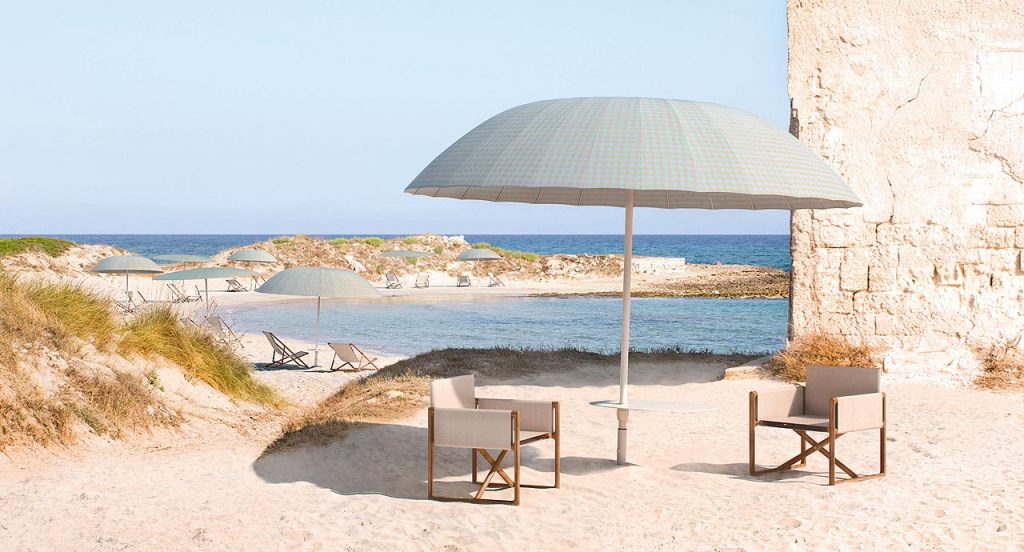 Two Portofino Outdoor Chairs with armrests and little armchair, structure and chair in natural heartwood, upholstered in beige fabric on a beach.