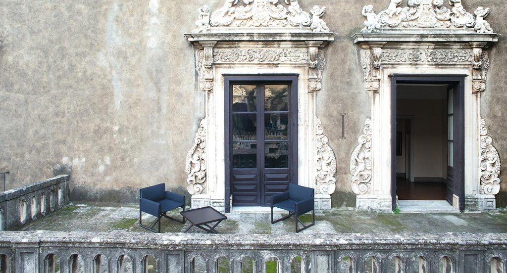 Two Portofino Outdoor Chairs with armrests and little armchair, structure and chair in natural heartwood, upholstered in blue fabric in a terrace.