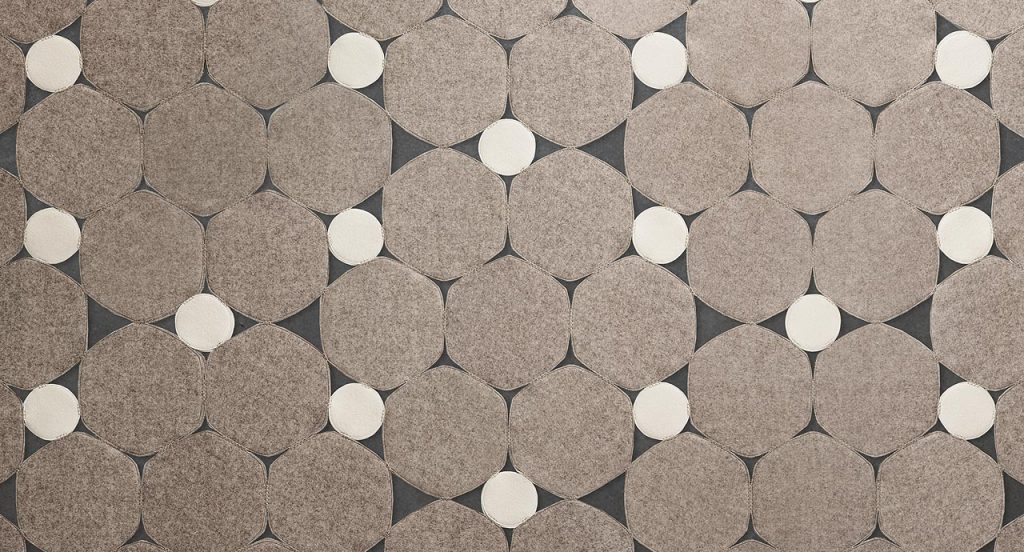 Prisma rug made by hexagonal, irregular forms in grey and white felt on a grey background.