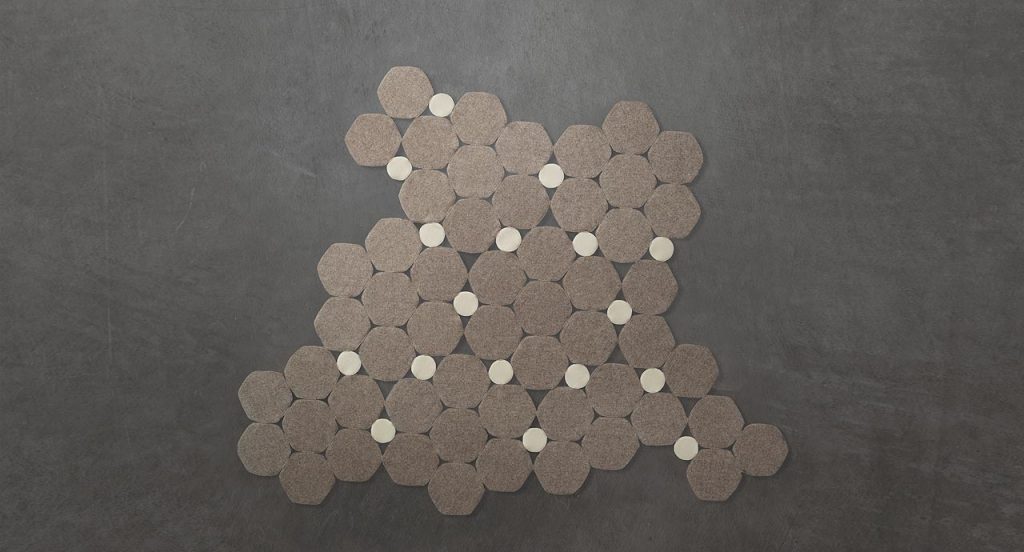 Prisma rug made by hexagonal, irregular forms in grey and white felt on a grey background.