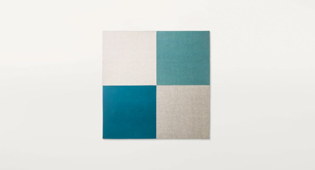 Quadri rug made with white, grey and blue felt squares on a white background.