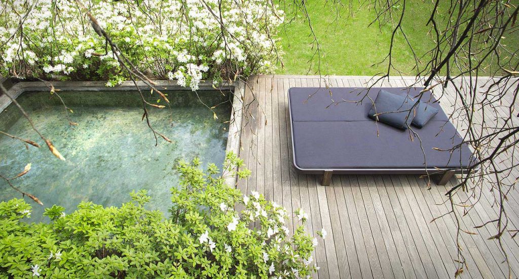 Double Rams sun bed with backrest, four legs in brown wood, cover in blue polyester next to a pool.