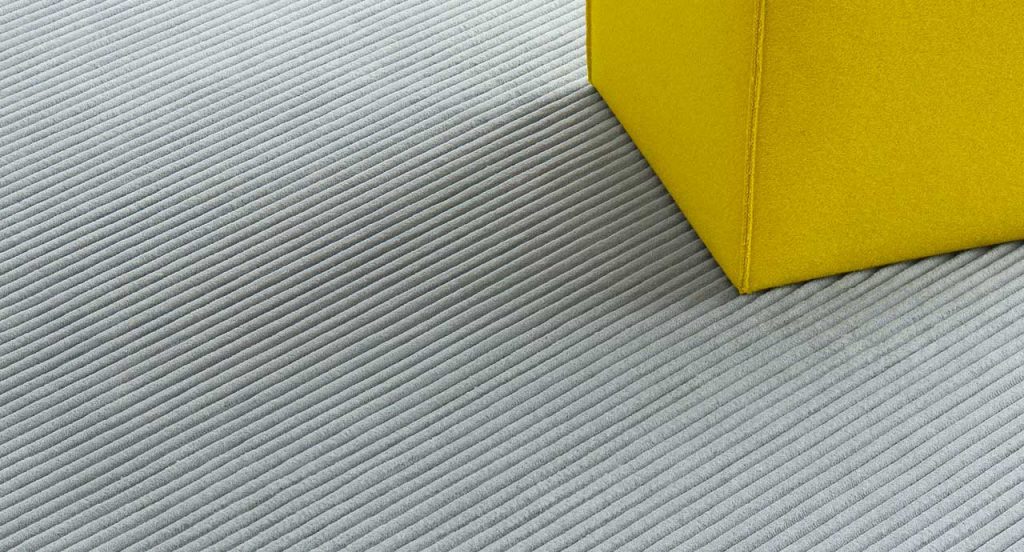 Grey Raya rug with parallel lines in relief with a pouf.