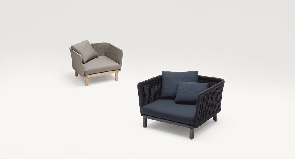 Two Sabi Armchairs, base and two legs made of natural wood, backrest in woven rope cord and cushion in fabric, one in black, one in beige on a white background.