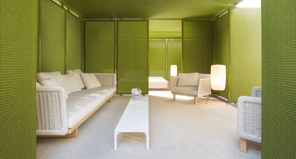 Two beige Sabi Armchairs, base and two legs made of natural wood, backrest in woven rope cord and cushion in fabric in a living room.