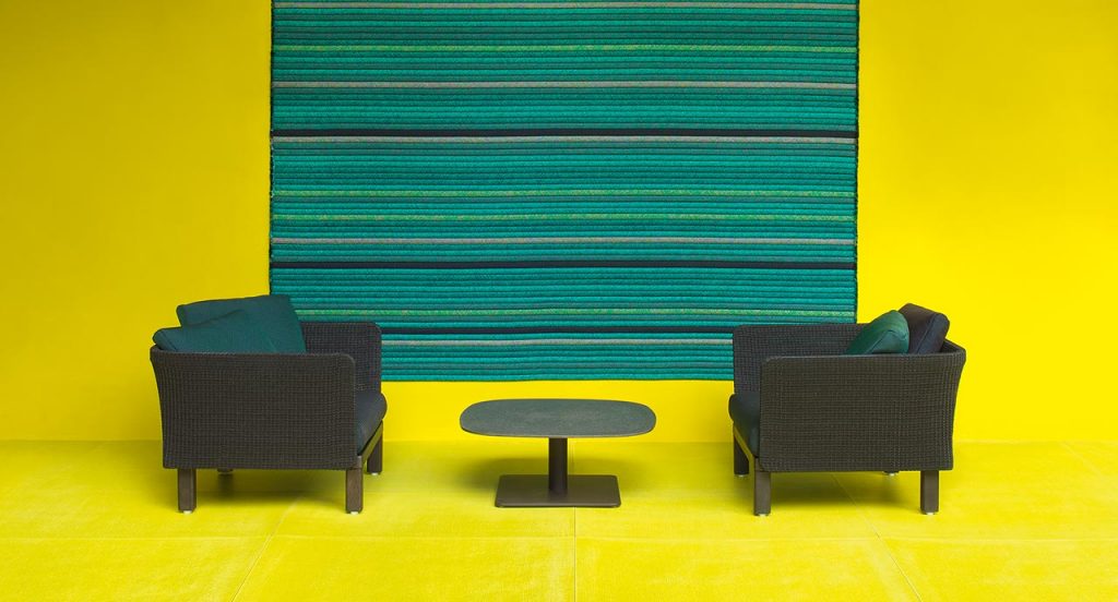 Two black Sabi Armchairs, base and two legs made of natural wood, backrest in woven rope cord and cushion in fabric on a yellow room.