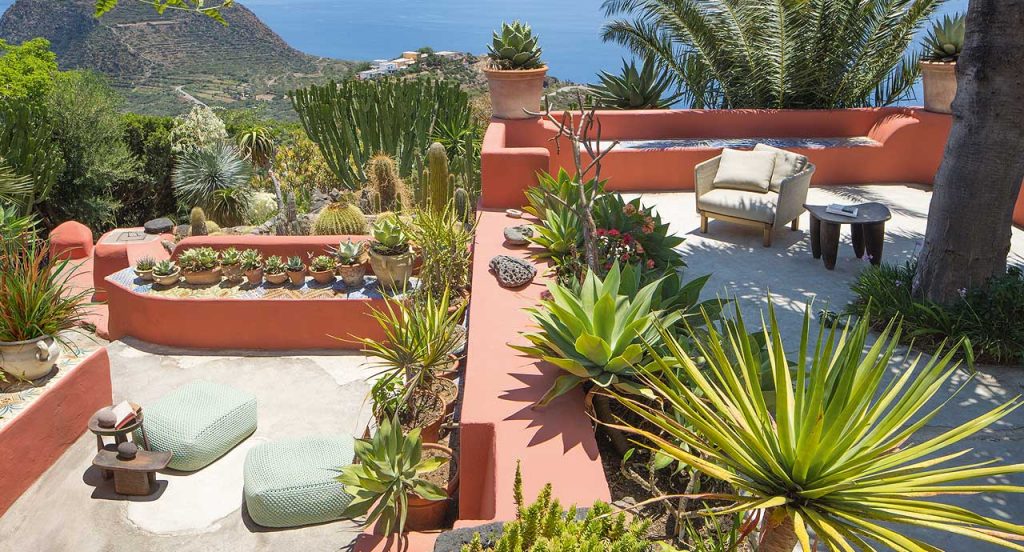 Beige Sabi Armchair, base and two legs made of natural wood, backrest in woven rope cord and cushion in fabric in a terrace.