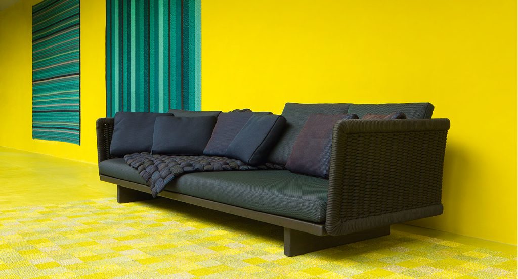 Sabi Sectional, base and two legs in natural wood, upholstery in black fabric on a yellow room.