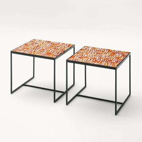 Two square Segni side tables, structure and two legs in black steel, top in brown, orange, yellow ceramic lines on a white background.