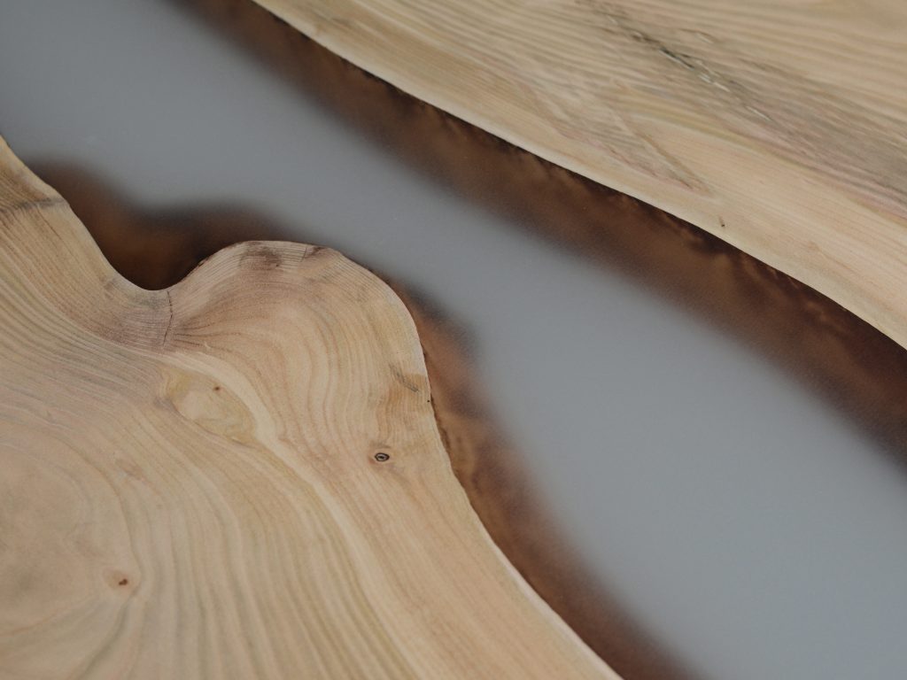 Closeup of Creek Table with a rectangular shape, made of solid walnut wood with a natural finish and featuring a transparent resin inlay, set against a white background.
