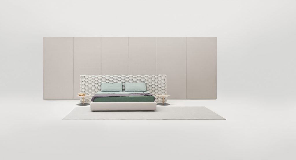 Silent bed with headboard. Cover in white fabric , headboard in white chain tubular polyester knit in a bedroom.