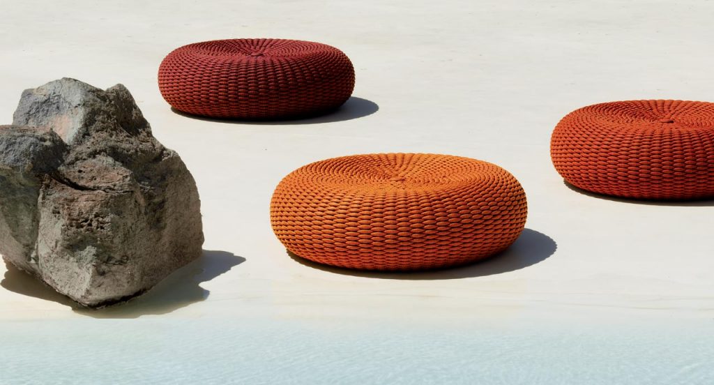 Three Shell poufs, upholstery in rope, one in red and to in orange nexto to a pool.