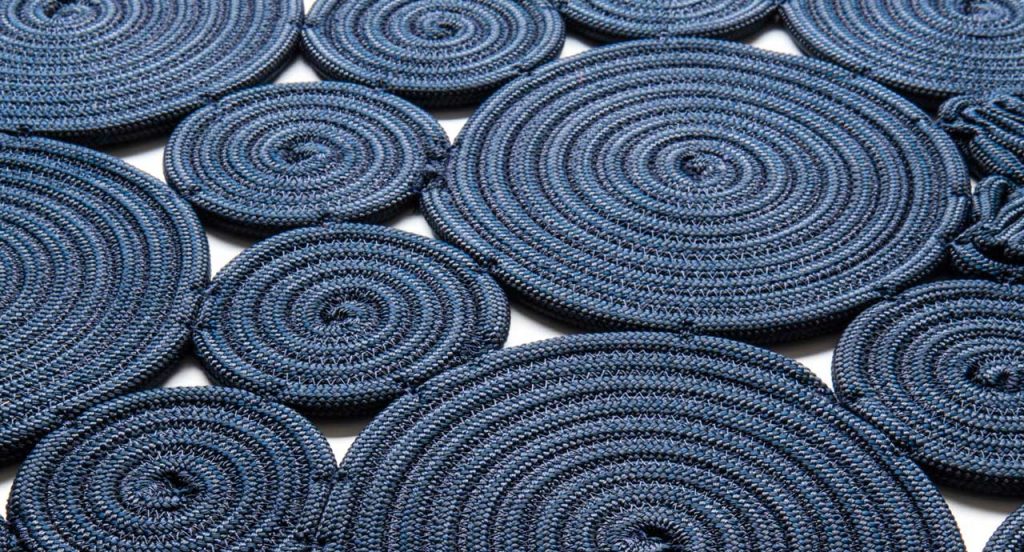 Spin off rug, made of blue sewn spirals on a white background.