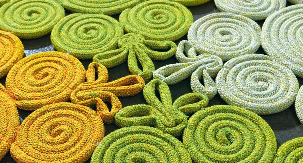 Spin Rug made of white, green and yellow sewn spirals and leaves on a grey background.