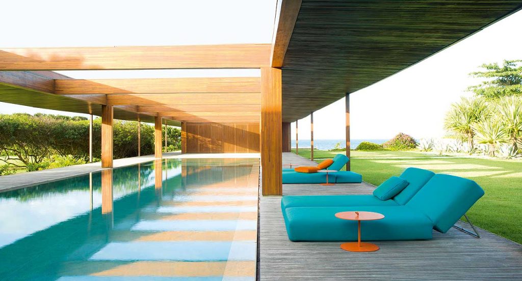 Three Swell sun beds, structure in steel, upholstery in blue fabrics next to an oudoor pool.