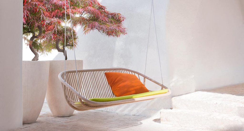 Swing suspended seat, structure in natural wood, pink seat pad, orange loose cushions and suspension cords on a white background.
