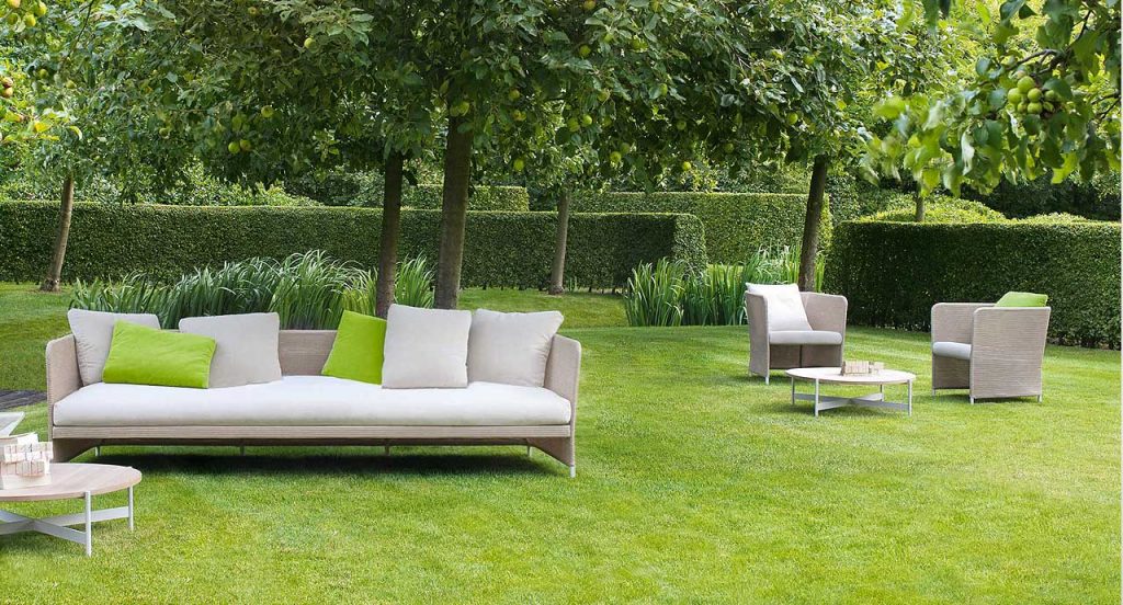 Two brown Teatime Armchairs, upholstery in Thuia fabric, two cushions and four steel legs in the countryside.
