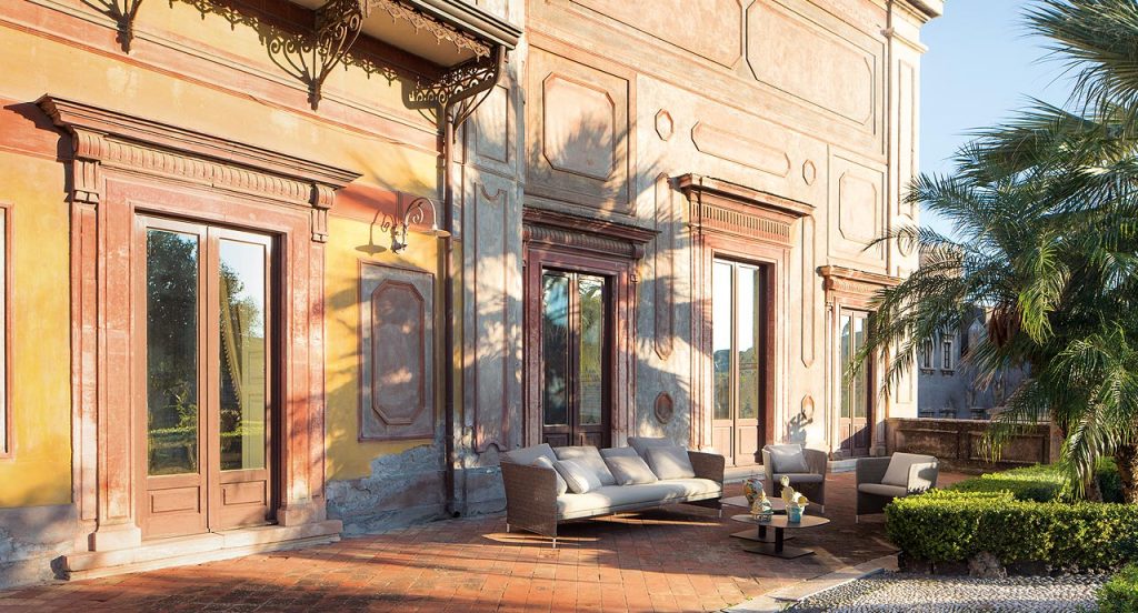 Two brown Teatime Armchairs, upholstery in Thuia fabric, two cushions and four steel legs in the countryside.