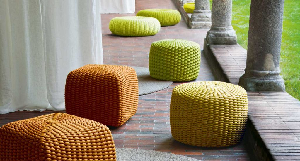 Four Tide poufs, two in orange, one in yellow, one in green upholstery woven with Rope cord in an outdoor place.