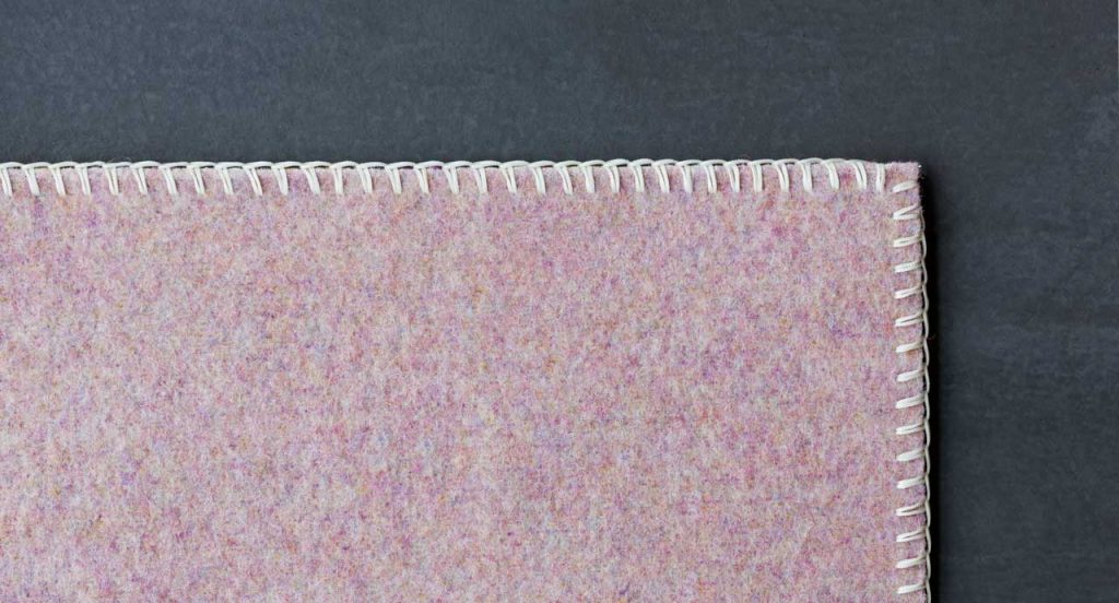 Pink Unito rug made of two layers of felt with punyo cavallo border stitching on a grey background.