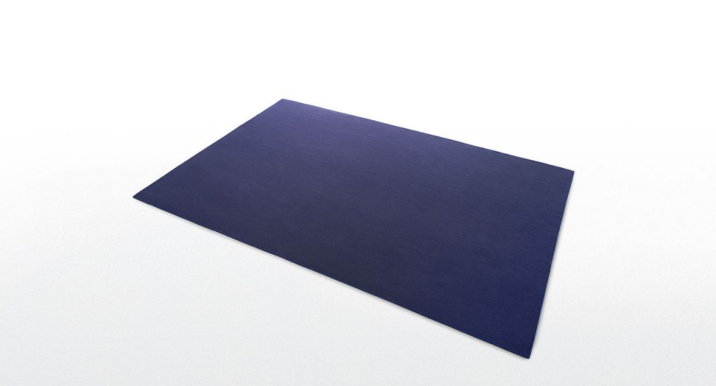 Blue Unito rug made of two layers of felt with punyo cavallo border stitching on a white background.