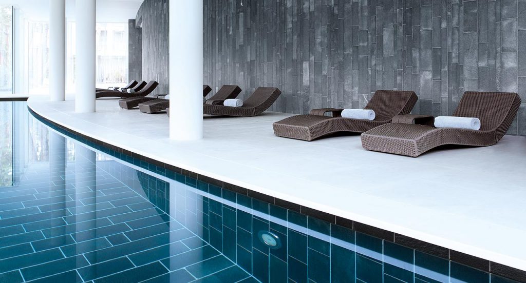 Nine brown Wave chaise loungers in rope cord next to an indoor pool.