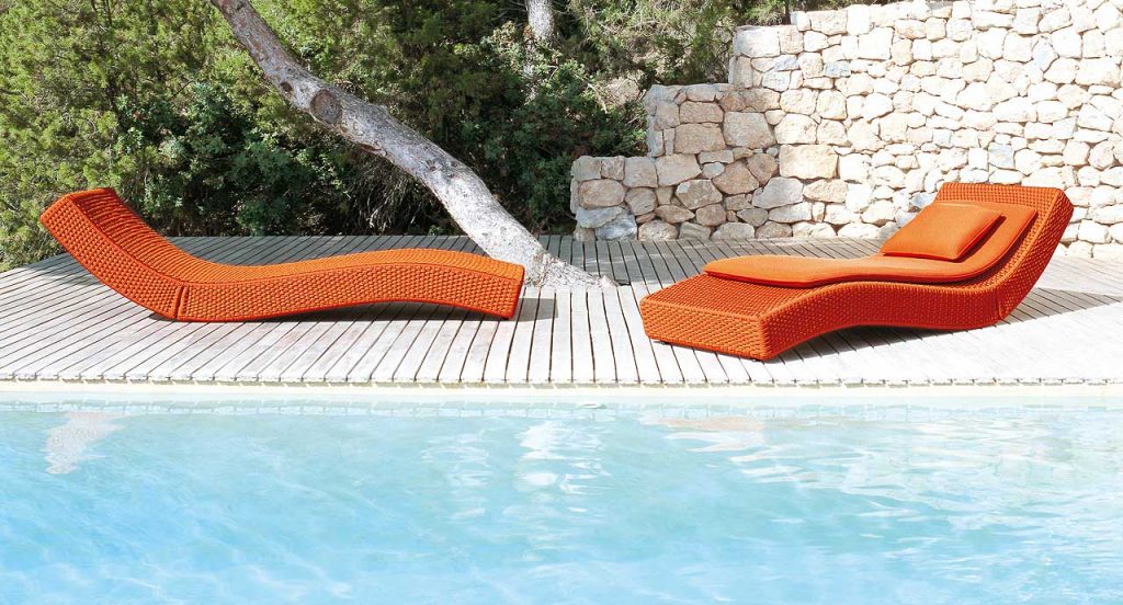 Two orange Wave chaise loungers in rope cord next to an outdoor pool.