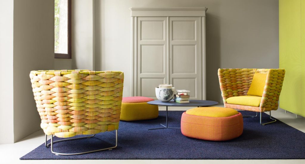 Two Smile Indoor Pouf, upholstered in blend y dots fabric , one in red and yellow, one in orange and yellow in a living room.