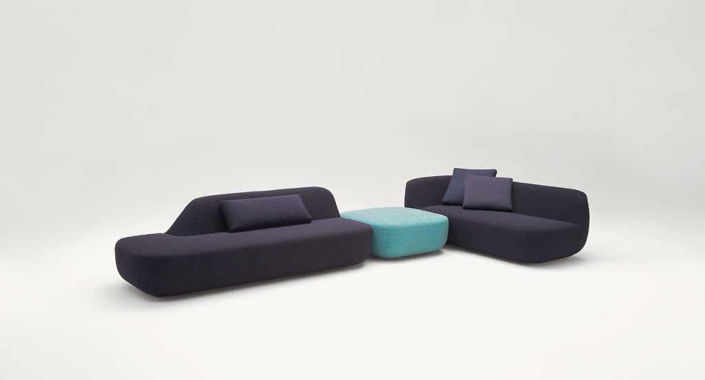 Uptown Pouf, blue fabrics upholstery in the middle of two sofas on a white background.