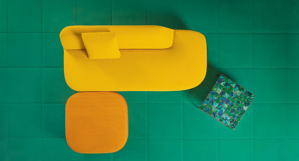 Uptown Pouf, yellow fabrics upholstery next to a sofa on a white background.