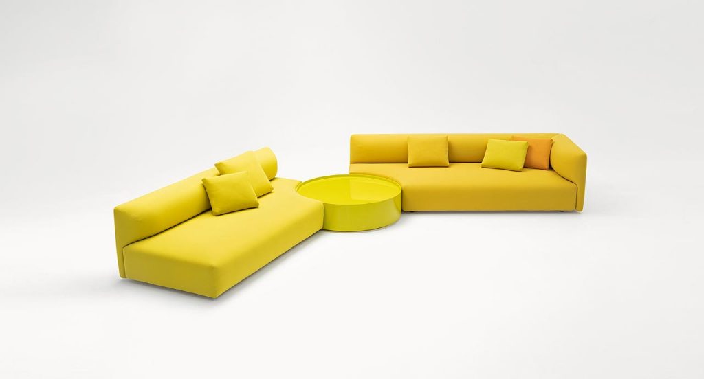 Yellow Walt Side Table with side opening and round shape with two sofas on a white background.