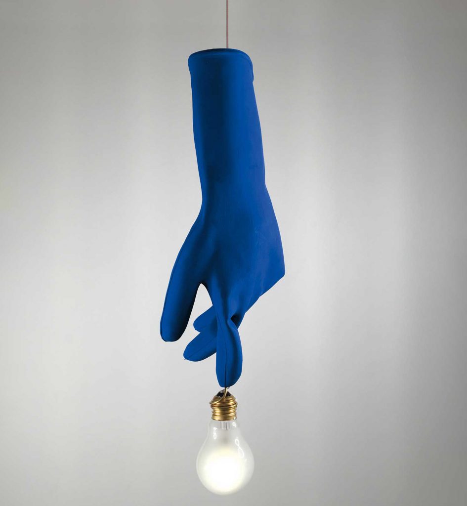 Luzy in blue illuminated hanging from a ceiling in front of a white wall