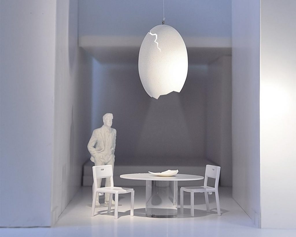 A white room with a table and chairs with a Broken Egg lamp hanging over the table