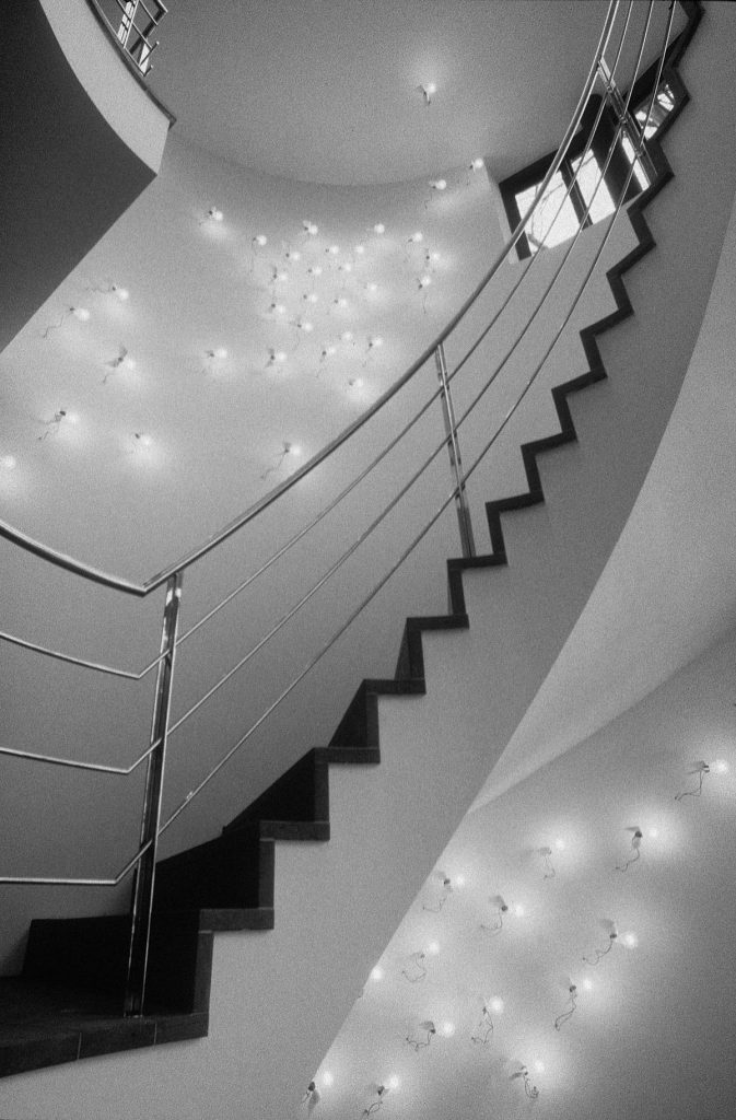 A black and white photo of a spiral staircase with Lucellino Wall lights on top and below the staircase