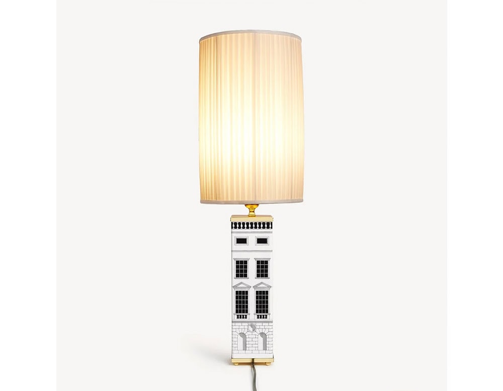 A distinctive lamp with a glowing pleated shade and a strikingly illustrated base inspired by architectural elements, blending artistic design with functional lighting.
