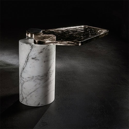 A contemporary coffee table featuring a cylindrical white marble base and a hand-textured metallic top, blending elegant materials with sculptural balance in a striking minimalist design.