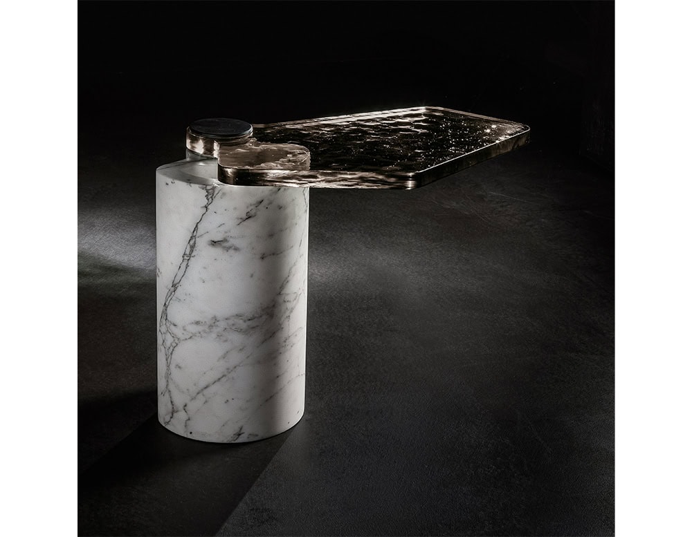 A sculptural coffee table featuring a cylindrical white marble base supporting a textured metallic top, blending organic elegance with modern craftsmanship in a striking, minimalist composition.