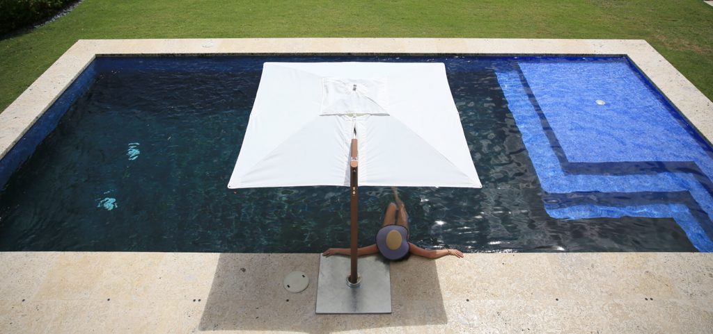 pool umbrella made of fabric and wooden base with maztiles in a brown tone and white fabric in a pool