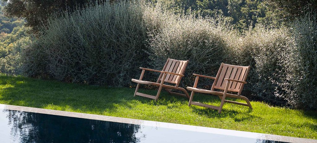 Two Levante Seven Lounge Chair in front of a pool with bushes in the background