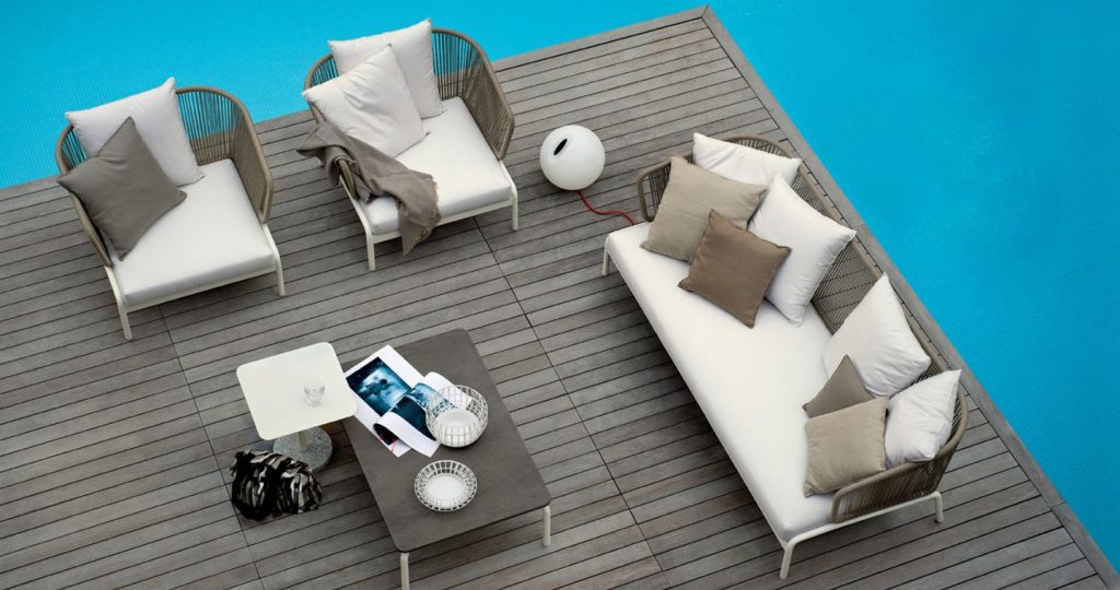 Top view of a pair of Spool One Sofa on a deck with a larger sofa to the side with a coffee table in the middle of the deck with a pool surrounding the sides