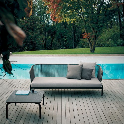 Spool Three Sofa in front of a pool on a grey colored deck with some fall trees in the background