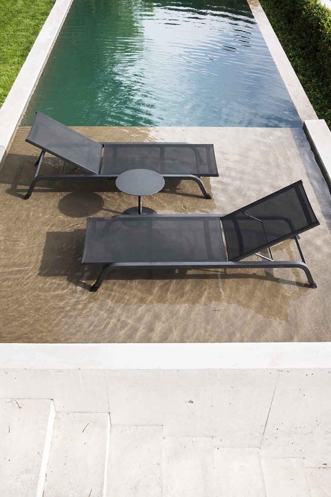 Pair of Surfer One Sunlounger in grey facing towards each other with a side table in between next to a pool