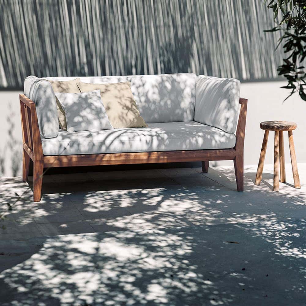 Teka One Sofa in white on a patio with a grey wall in the background and a side table next to the sofa