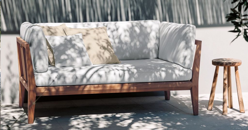 Teka One Sofa in white on a patio with a grey wall in the background and a side table next to the sofa