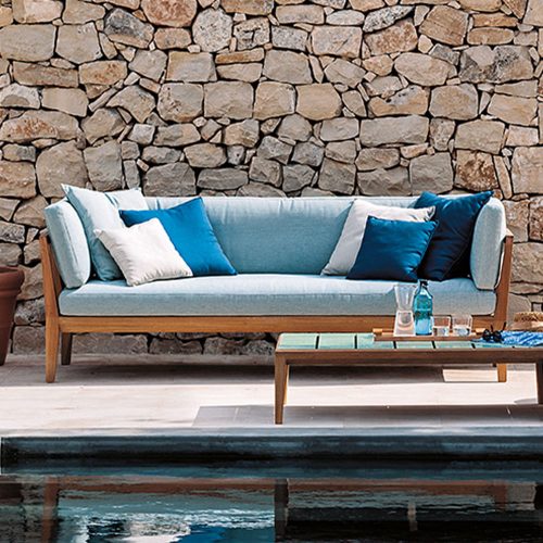 Teka Two Sofa behind a pool with a stone wall behind