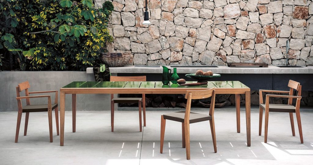 Quad Teka One Hundred Seventy One Armchair surrounding a wood table in front of a stone wall on a patio