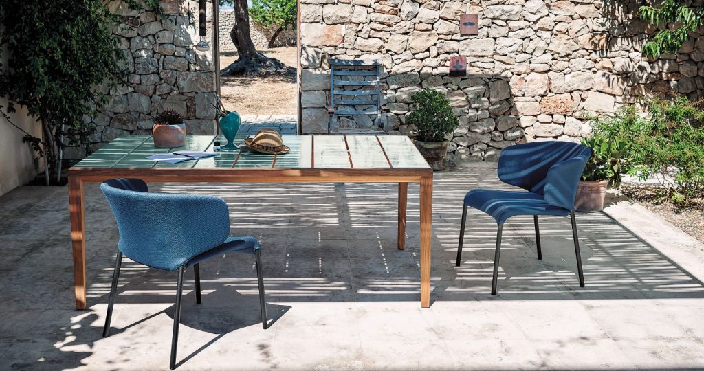 Teka One Hundred Seventy Three Table on a patio with two chairs on either side with a stone wall in the background