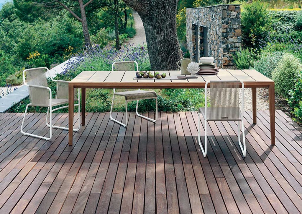 Teka One Hundred Seventy Four Table with two chairs surrounding the table on a deck with trees and grass in the background
