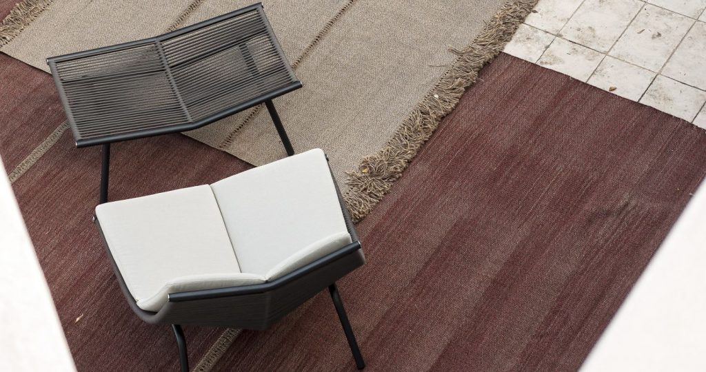 Triptyque Two Rug on a dark brown wood floor with a chair next to the rug with a book on top of the seat